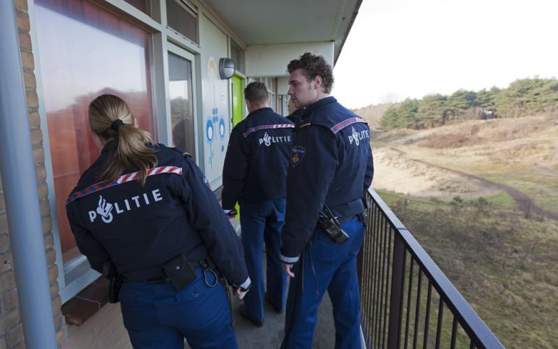 Drie politieagenten bij een woning, natuur op de achtergrond