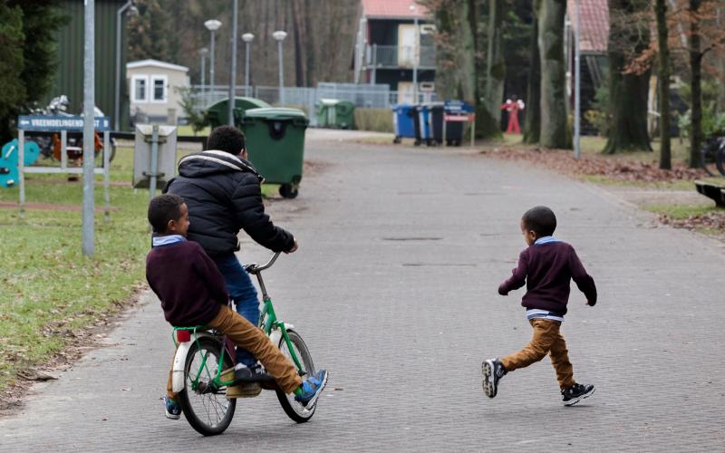 Drie spelende kinderen in het AZC, rennend en op de fiets