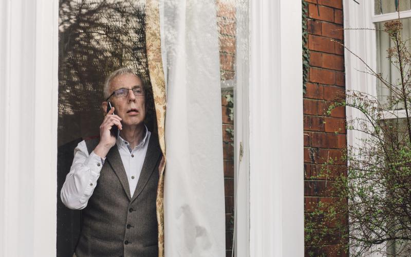 Een oudere man bij het raam met telefoon
