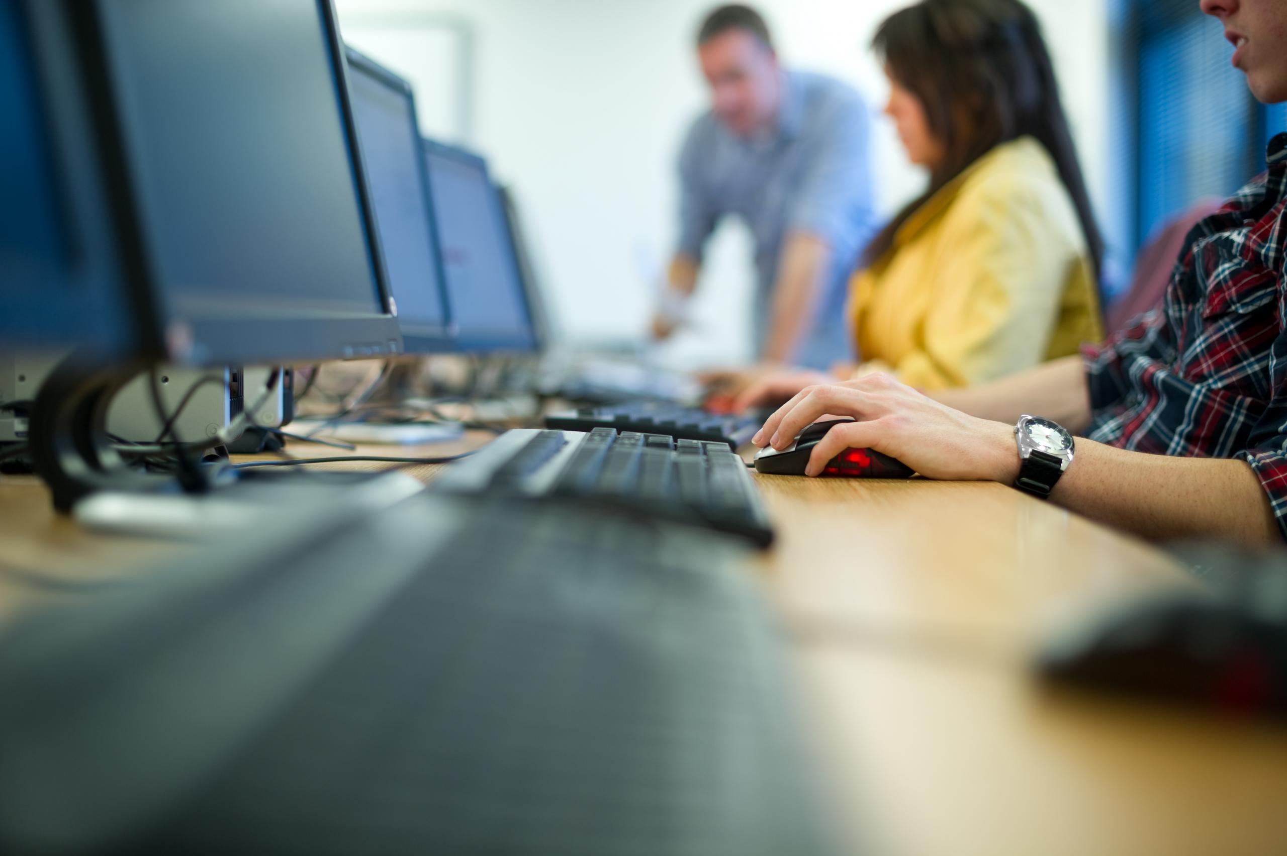 Foto van een rij computerschermen met daarachter mensen