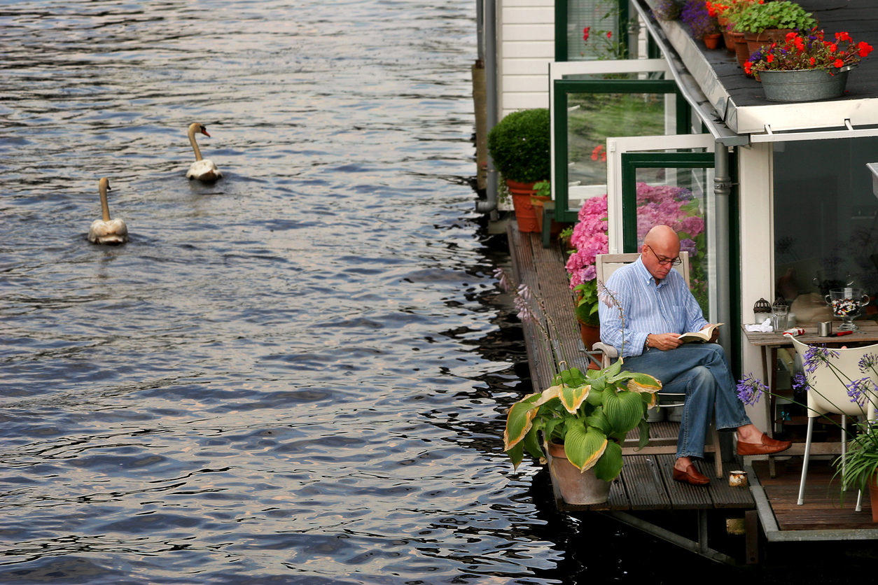 man leest boek op terras van woonboot