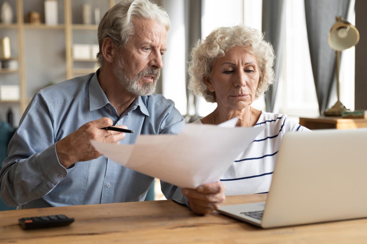 Ouder echtpaar leest een brief en zit achter de laptop