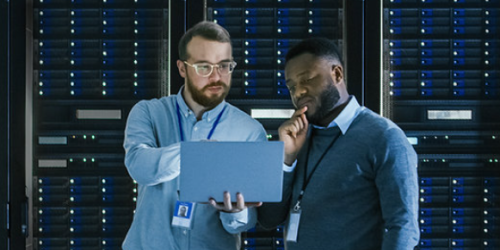 Twee mannen staan voor een dataopslagmuur, en kijken samen naar een laptop