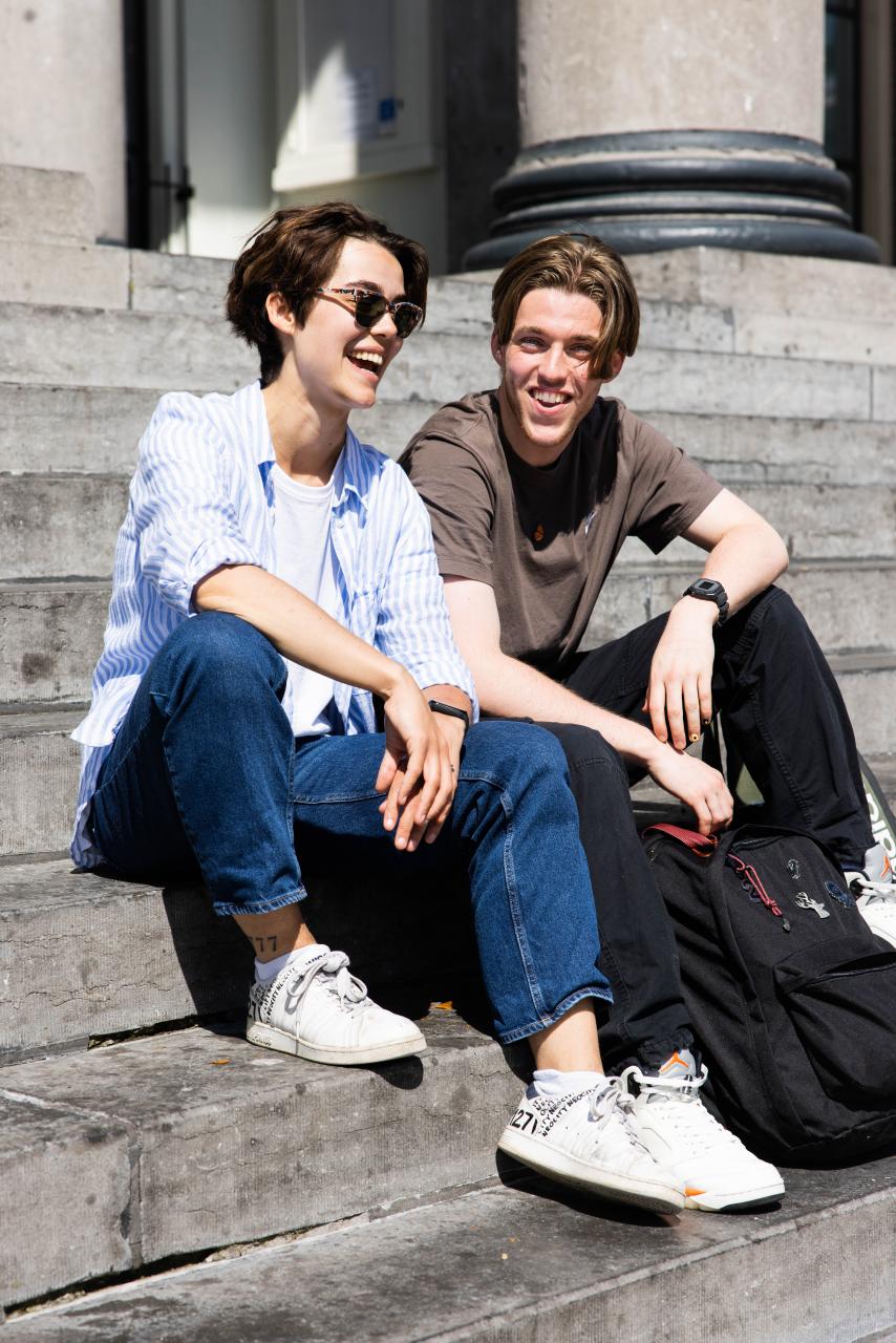 Romein en KlaasJan, twee jongeren van in de twintig zitten op een trap en lachen.