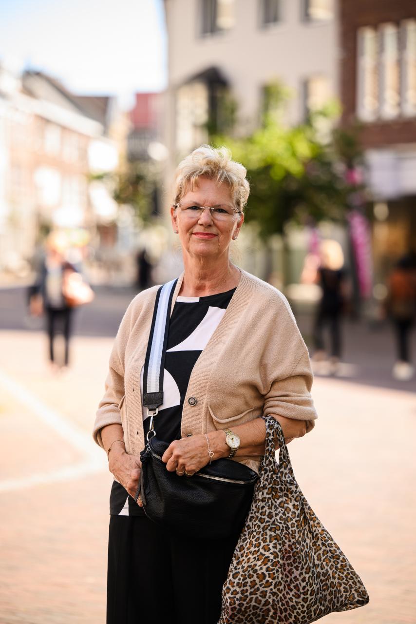 Een vrouw met kort blond haar staat in een winkelstraat