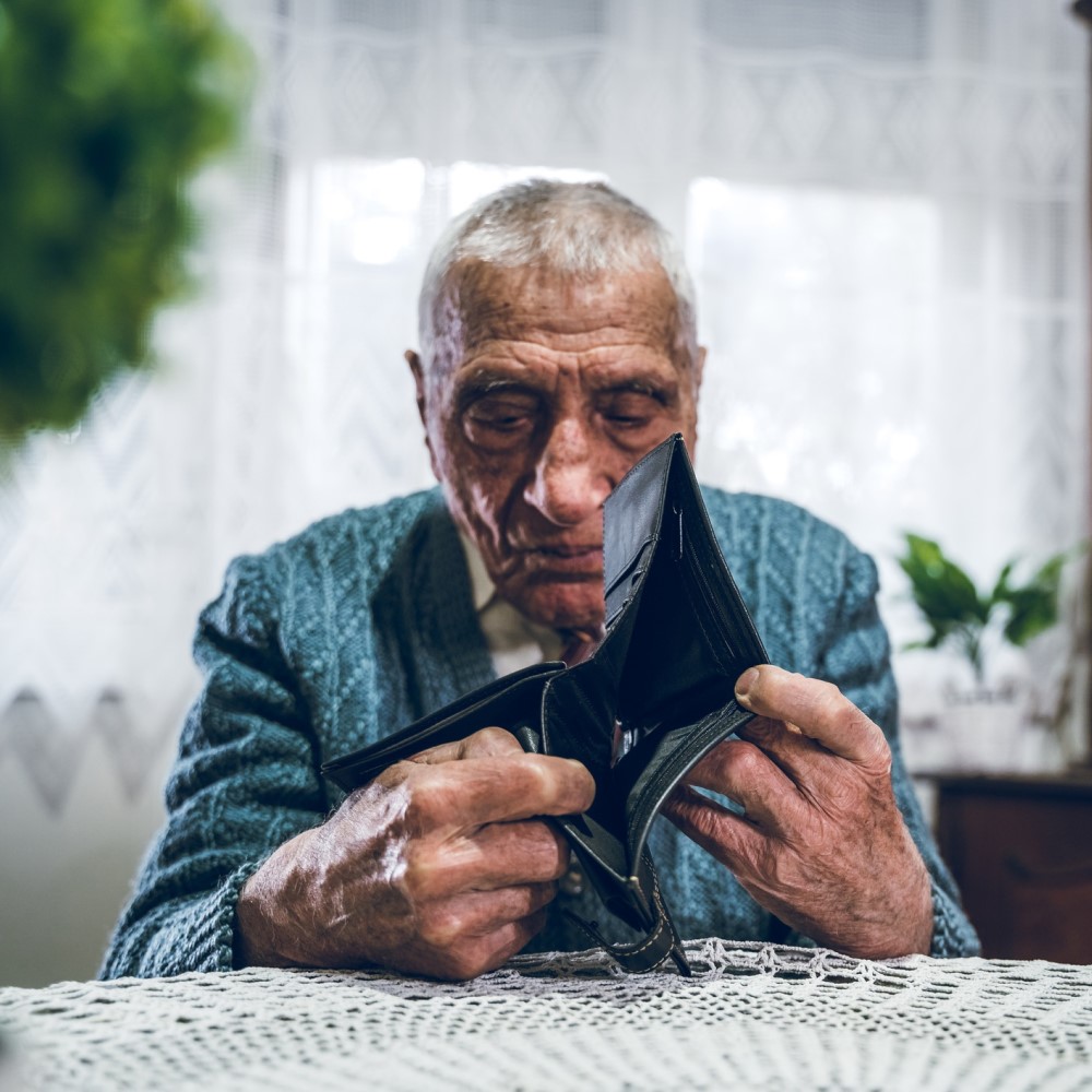 Een bejaarde man zit aan tafel met een lege portemonnee in zijn handen.