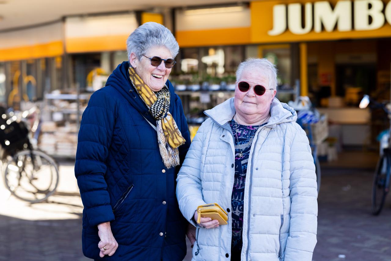 Jacoba en Mary, twee gepensioneerde vrouwen staan op straat voor een supermarkt.
