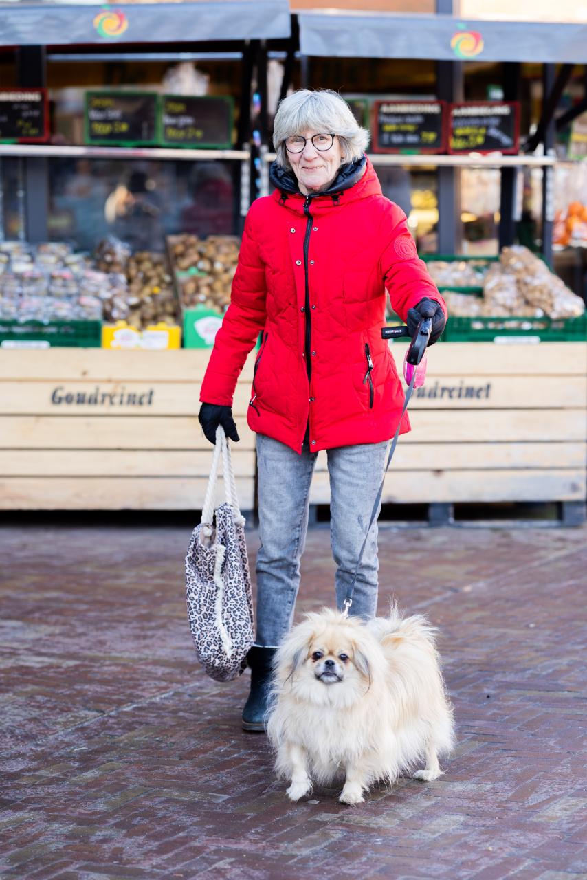 Tineke, een gepensioneerde vrouw op straat met een tas in haar hand en haar hondje.