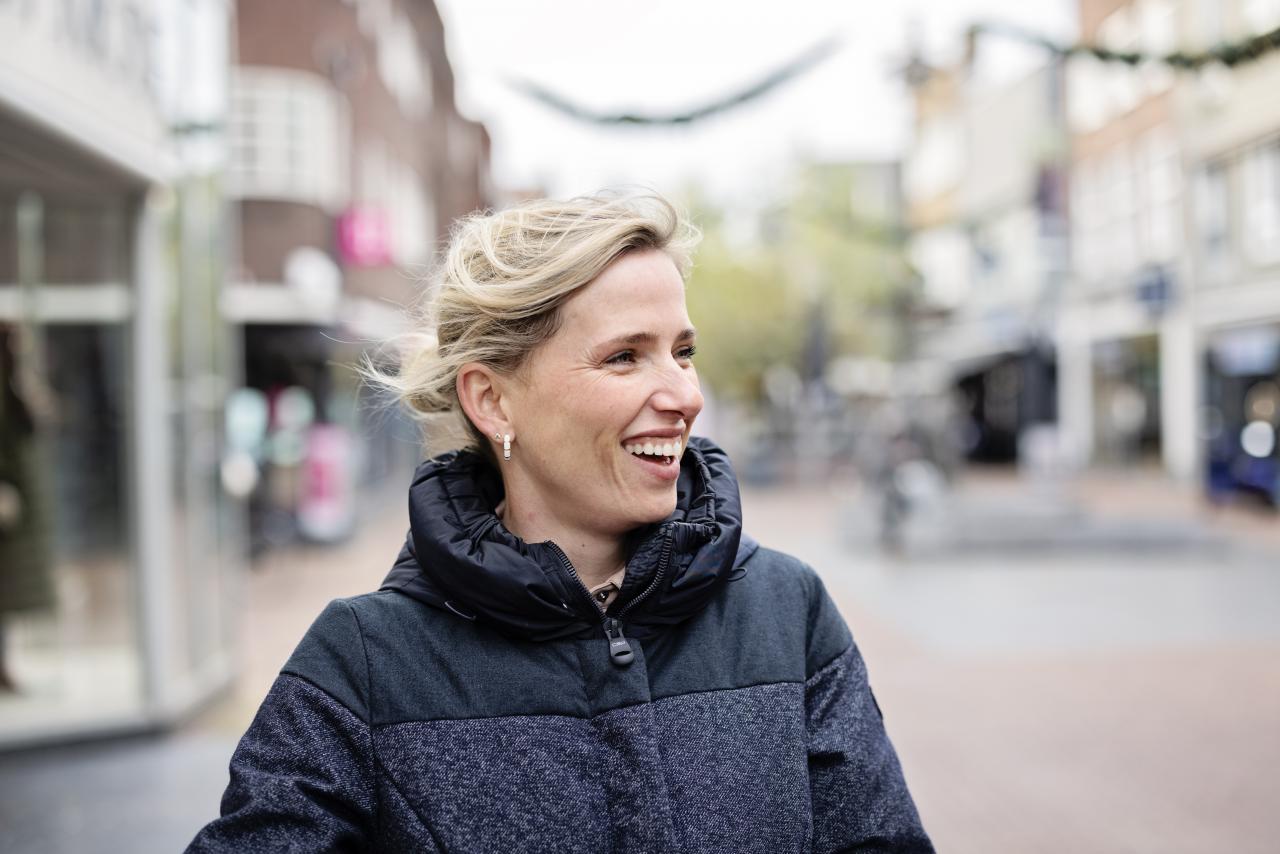 Vrouw van middelbare leeftijd met blond haar kijkt lachend naar rechts.