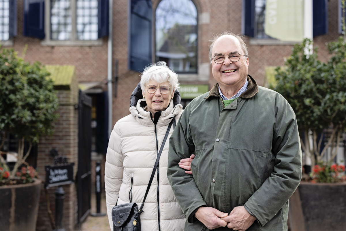 Een oudere man en vrouw poseren samen voor een foto. De vrouw heeft de arm vast van de man.