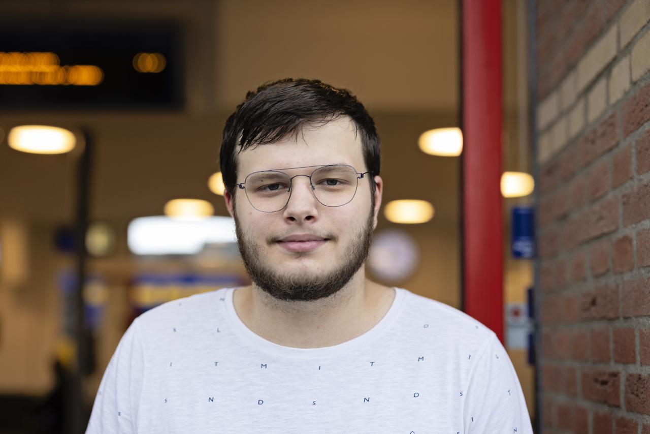 Een jonge man met een wit t-shirt aan kijkt in de camera