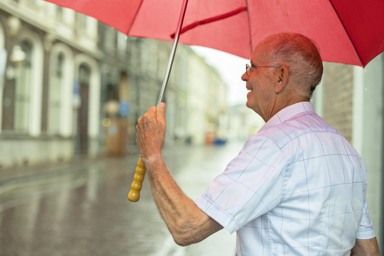 Een oudere man met een rode paraplu in zijn hand.