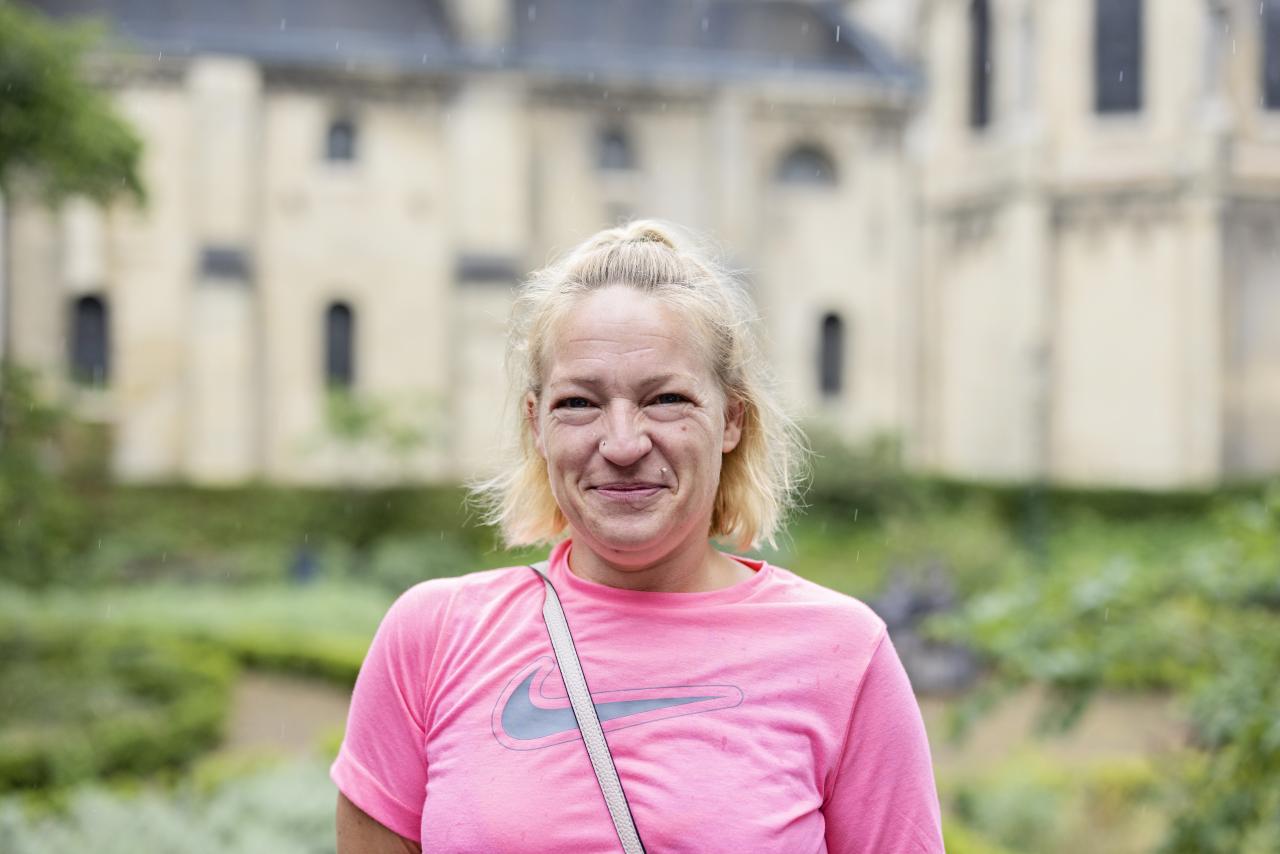 Een glimlachende vrouw van middelbare leeftijd met een roze t-shirt aan. Ze kijkt in de camera.