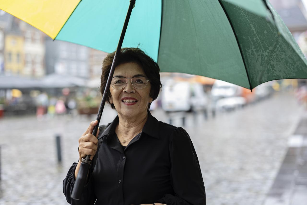 Een oudere vrouw met bril houdt kleurrijke paraplu vast. 