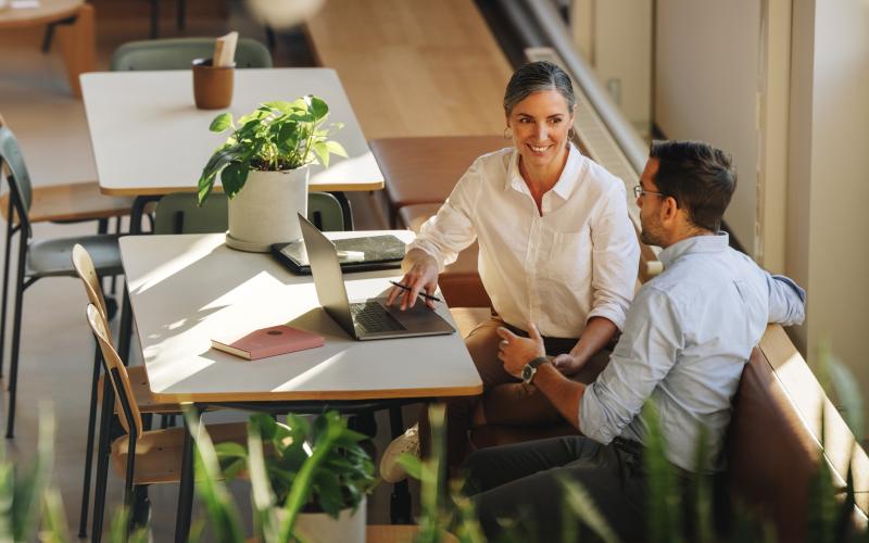 Twee professionals in een cafe samen aan het werk. Je ziet ze van veraf aan tafel zitten. Een vrouw links en een man rechts. Twee professionals in een cafe samen aan het werk. Je ziet ze van veraf aan tafel zitten. Een vrouw links en een man rechts.