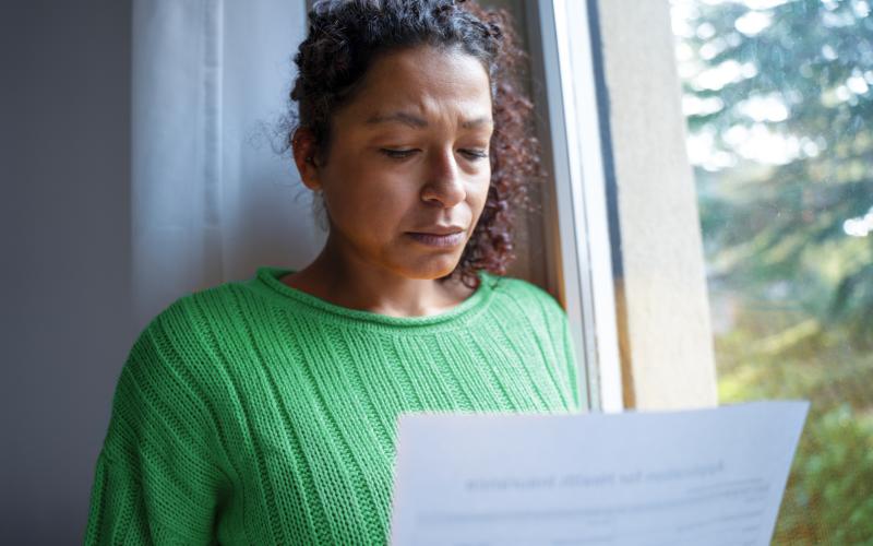 Vrouw met groene trui staat voor raam. Ze leest een brief