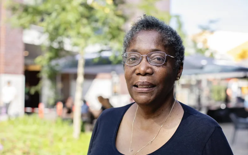 Portret van senior vrouw. Ze draagt een zwarte top en heeft een bril op.