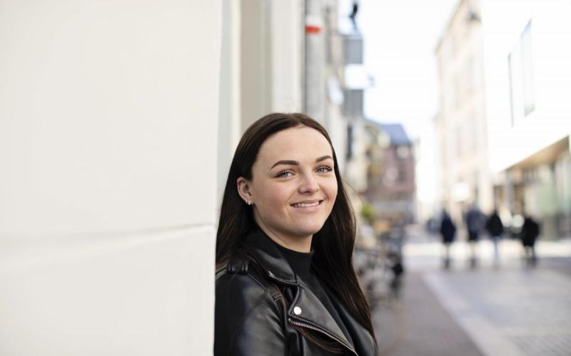 Portret van jonge vrouw. Ze staat op straat tegen een muur geleund, heeft donker haar en een zwart leren jasje aan. Portret van jonge vrouw. Ze staat op straat tegen een muur geleund, heeft donker haar en een zwart leren jasje aan.