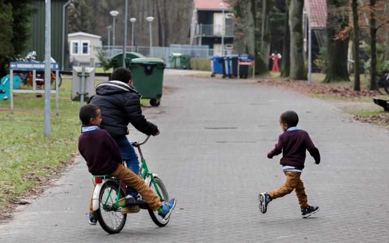 Drie spelende kinderen in het AZC, rennend en op de fiets Drie spelende kinderen in het AZC, rennend en op de fiets