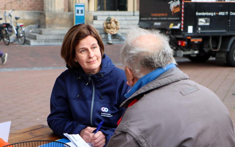 Een medewerker van de Nationale ombudsman in gesprek met een man op straat Een medewerker van de Nationale ombudsman in gesprek met een man op straat