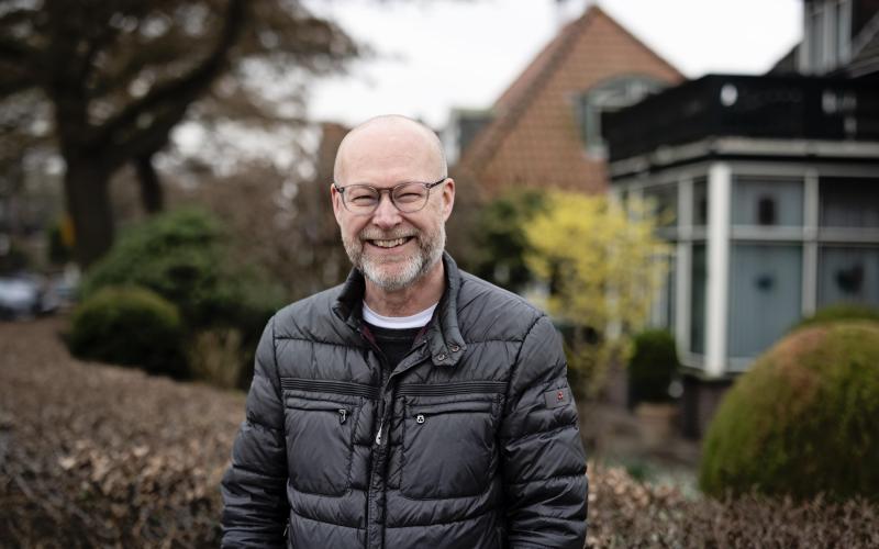 Een man staat lachend voor een tuin en poseert voor de foto