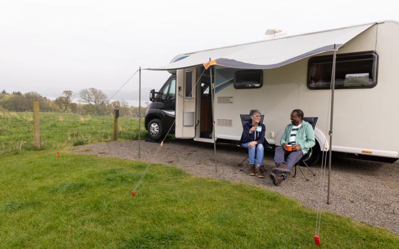 Een vrouw en een man zitten voor een camper op twee campingstoelen. Ze zijn in gesprek. Een vrouw en een man zitten voor een camper op twee campingstoelen. Ze zijn in gesprek.