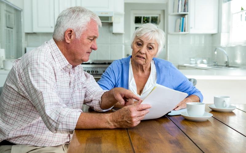 Ouder echtpaar zit aan de keukentafel en leest samen een brief.