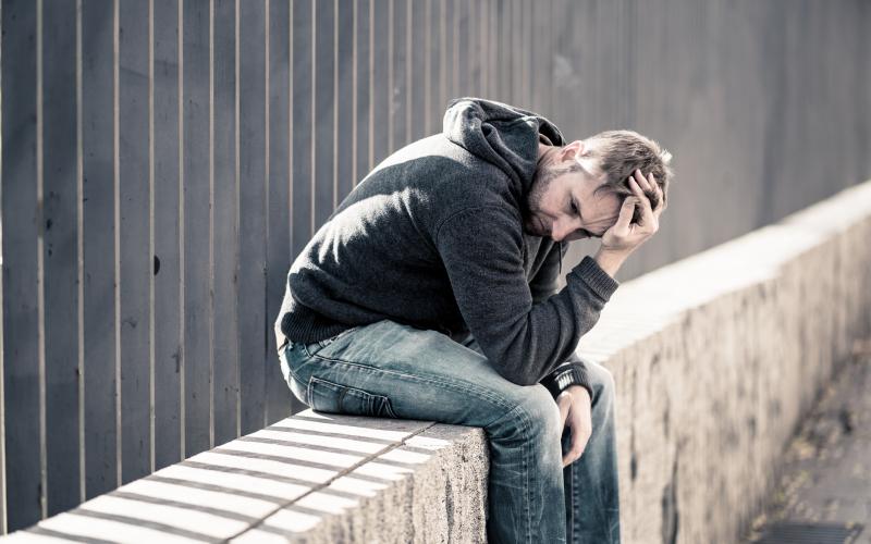 Man zit op muur en houdt zijn hoofd in de handen. Hij kijkt treurig. Man zit op muur en houdt zijn hoofd in de handen. Hij kijkt treurig.