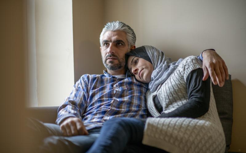 Een man en vrouw van islamitische afkomst zitten samen op de bank. Ze kijken bezorgd voor zich uit. Een man en vrouw van islamitische afkomst zitten samen op de bank. Ze kijken bezorgd voor zich uit.