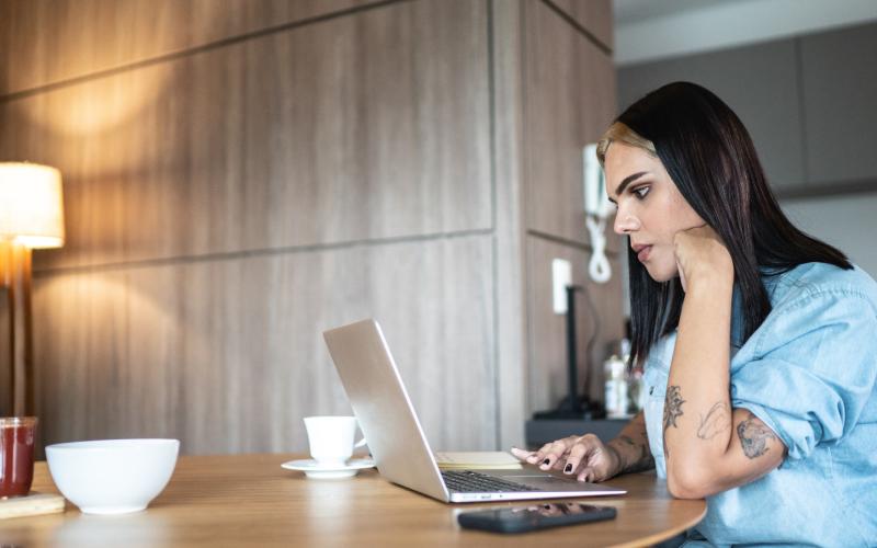 Een jongvolwassen vrouw zit achter haar laptop aan een keukentafel te werken.