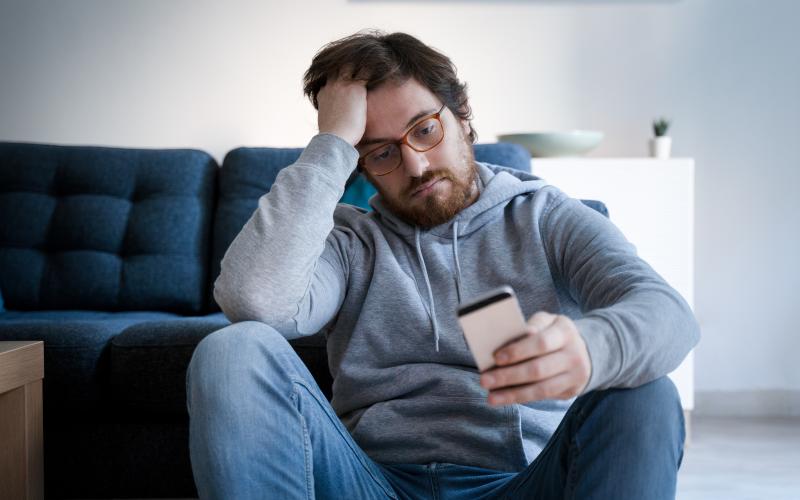 Man zit teleurgesteld op de grond voor zijn bank. Man zit teleurgesteld op de grond voor zijn bank.