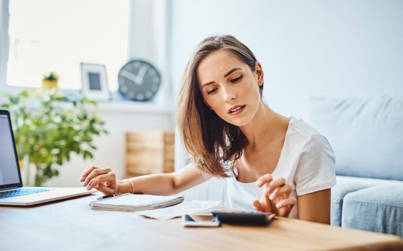 Vrouw zicht aan een tafel en heeft een rekenmachine en notitieblok voor zich