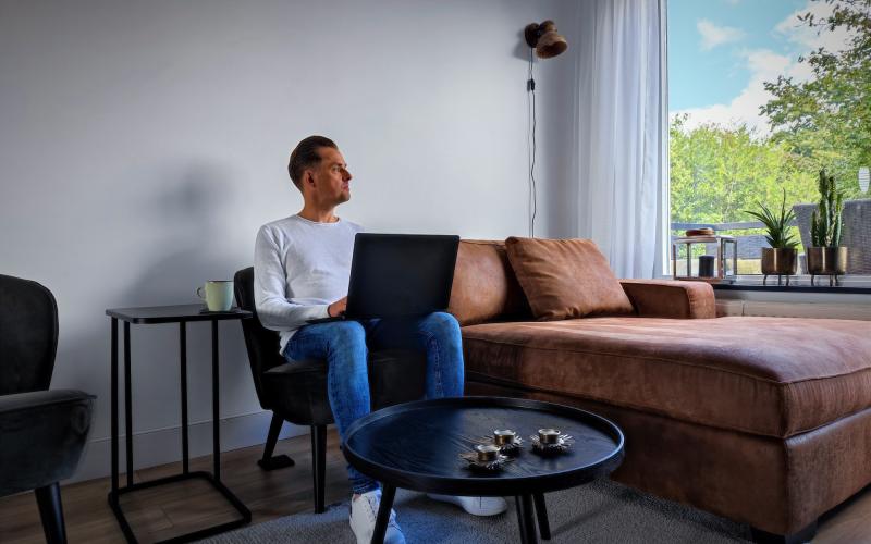 man met laptop in huiskamer kijkt naar buiten man met laptop in huiskamer kijkt naar buiten