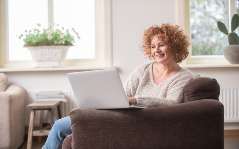 Vrouw met rood krullend haar zit op de bank en heeft haar laptop voor zich Vrouw met rood krullend haar zit op de bank en heeft haar laptop voor zich