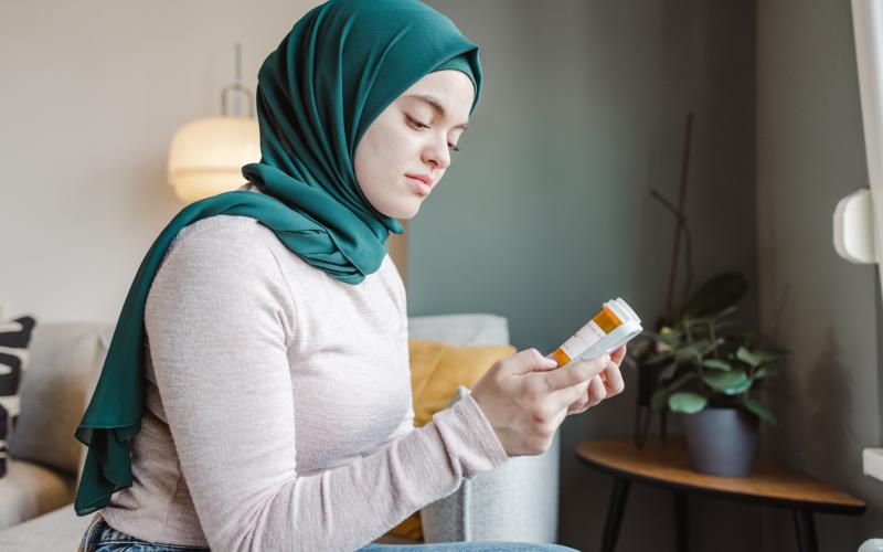 Jonge vrouw heeft een potje medicijnen vast en leest de beschrijving