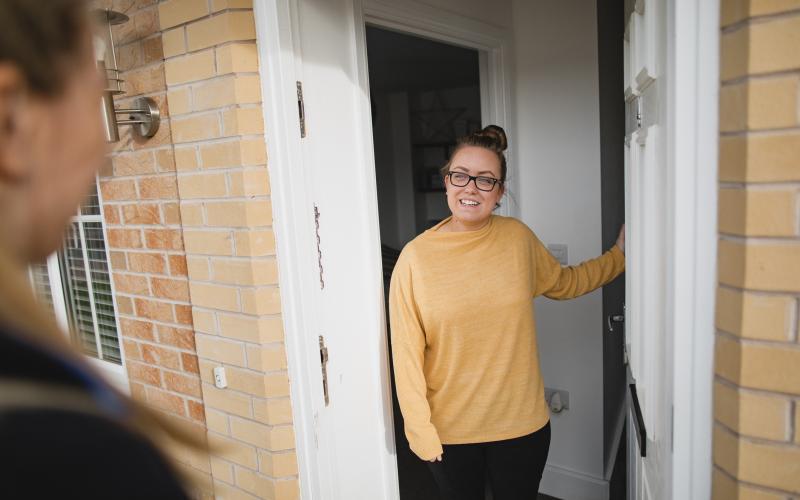 Jonge vrouw bij de voordeur doet open voor iemand