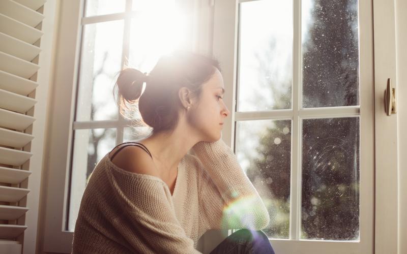 Jonge vrouw zit voor het raam en kijkt naar buiten