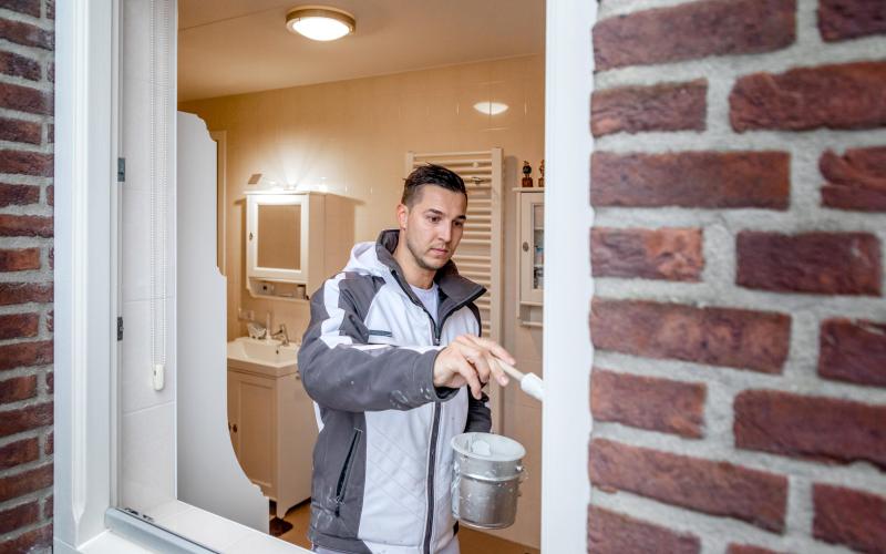 Een schilder staat in een raamkozijn en schildert het kozijn. Een schilder staat in een raamkozijn en schildert het kozijn.