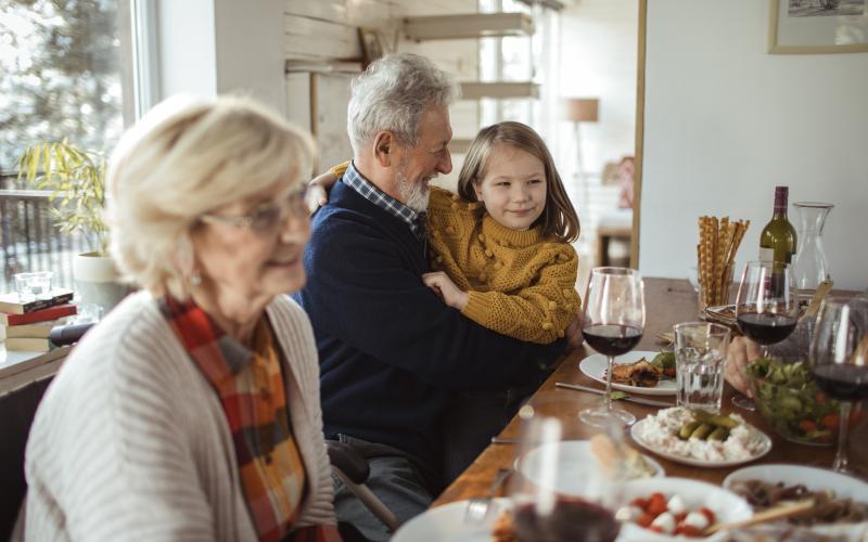 Senior vrouw en man, de grootouders, zitten aan een gedekte tafel met een van de kleinkinderen op schoot. Senior vrouw en man, de grootouders, zitten aan een gedekte tafel met een van de kleinkinderen op schoot.