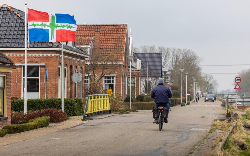 Een man op een gemotoriseerde fiets rijdt langs een aantal huizen in de provincie Groningen Een man op een gemotoriseerde fiets rijdt langs een aantal huizen in de provincie Groningen
