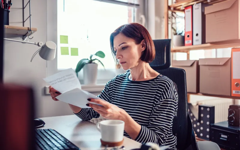 Vrouw met kort rood haar zit achter een bureau en leest een brief