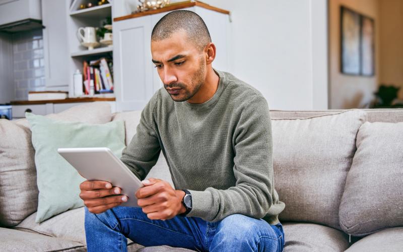 Man zit op de bank en kijkt serieus naar zijn tablet Man zit op de bank en kijkt serieus naar zijn tablet