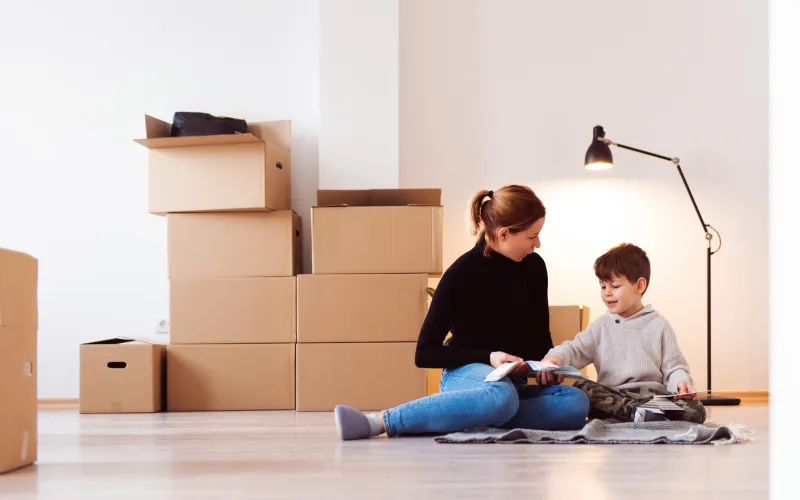 Moeder en zoon zitten op de grond in kamer. Op de grond staan verhuisdozen