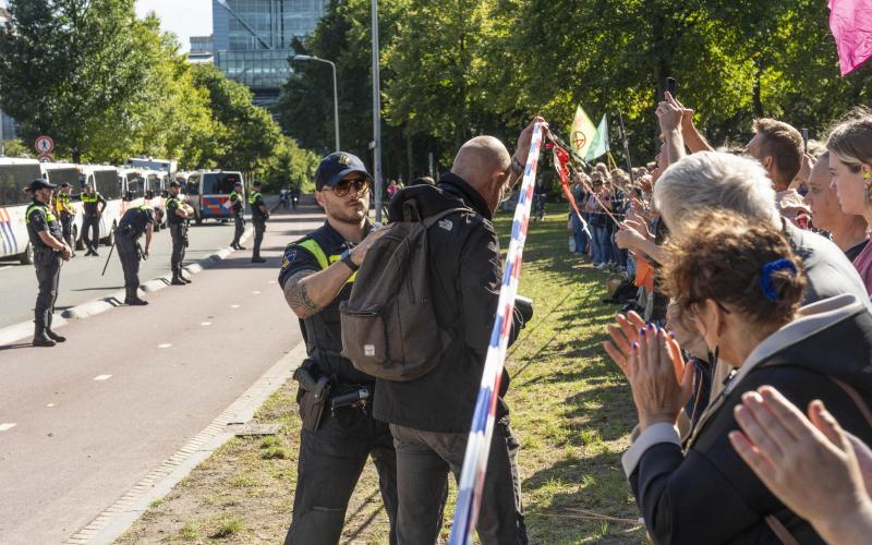 Een politieagent duwt een journalist achter een politielint Een politieagent duwt een journalist achter een politielint