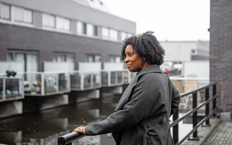 Vrouw van middelbare leeftijd staat bij haar huis aan het water