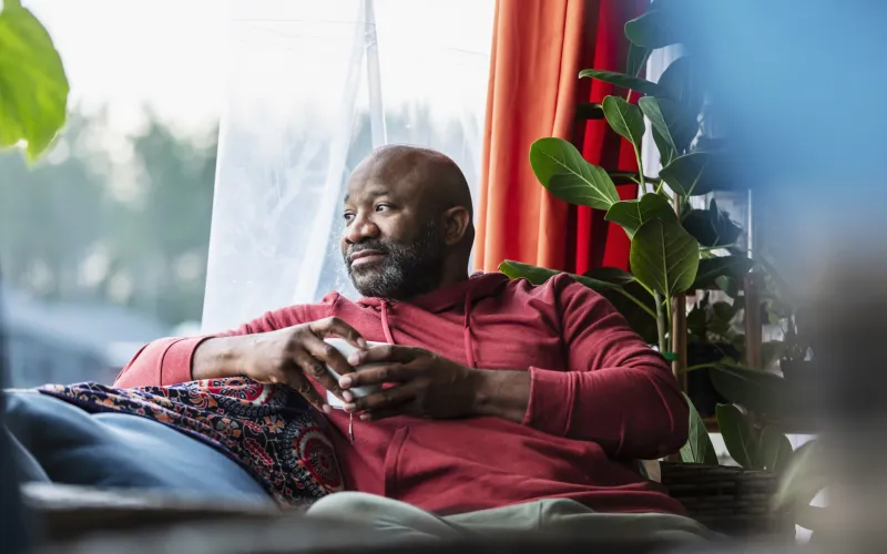 Man zit thuis op de bank achter een raam