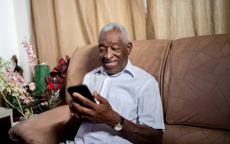 Senior gepensioneerde man zit op de bank met zijn smartphone