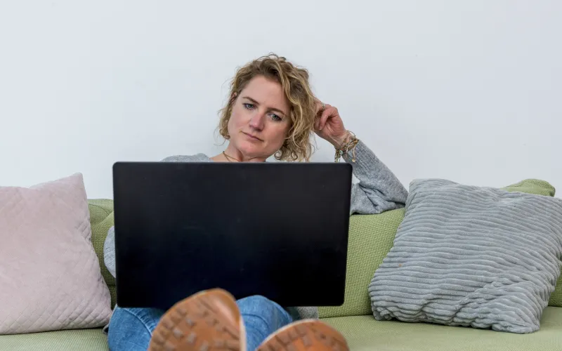 Vrouw zit op de bank met laptop op schoot