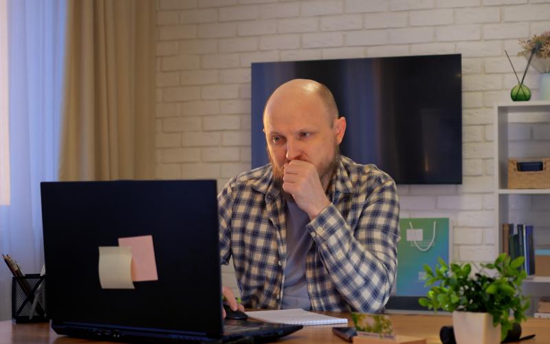 Man thuis achter laptop, hij kijkt bedenkelijk naar zijn scherm