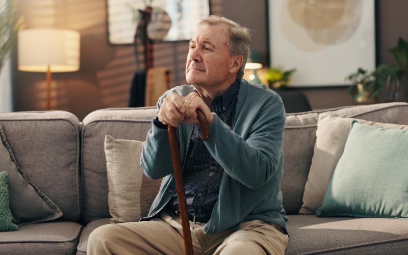 Senior man zit thuis op de bank met stok in zijn handen